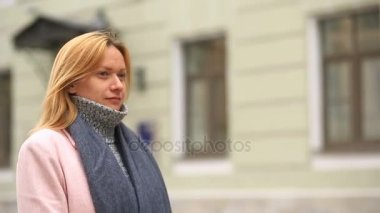 Bir pembe ceket ve kazak yorgun bir kadın kalabalık bir sokak ortasında duruyor ve soğuktan küçülür