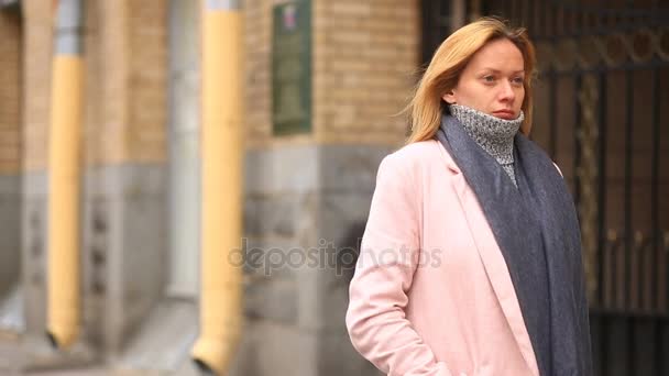 ピンクのコートとセーターで疲れた女性は混雑した通りの真ん中に立ってし、寒さから縮小 — ストック動画