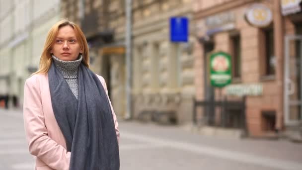 Eine müde Frau in rosa Mantel und Pullover steht mitten auf einer belebten Straße und schreckt vor der Kälte zurück — Stockvideo