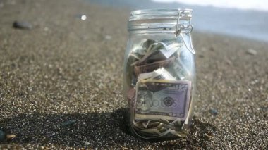 Bir cam kavanoz kağıt para dolar bir deniz dalgaları arka plan ile. Deniz ya da okyanus tarafından izinli tasarruf birikir. plaj