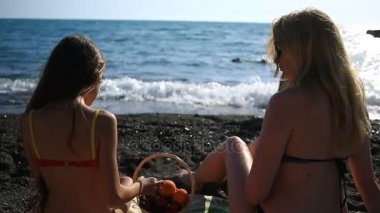 Anne ve kızı mayolu, uzun saçlı bir deniz plaj dalgalar bir arka plan üzerinde meyve ve çilek yeme