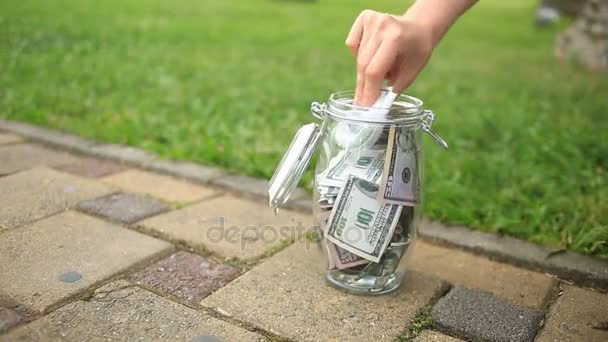 A person takes money from a glass jar on the street. Dollars in a glass jar — Stock Video
