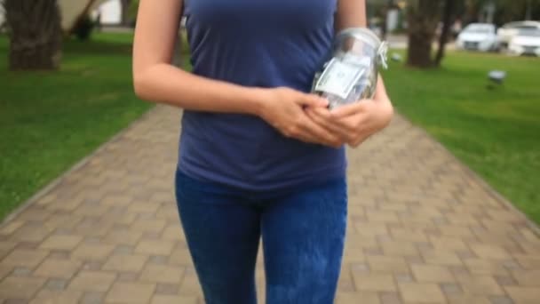 Mujer sosteniendo un frasco de vidrio con dólares en un fondo de calle de la ciudad — Vídeos de Stock