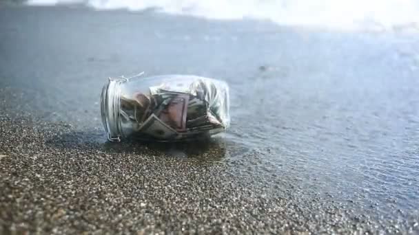 ขวดแก้วที่มีกระดาษเงินดอลลาร์กับพื้นหลังคลื่นทะเล สะสมเงินฝากออมทรัพย์เมื่อเดินทางโดยทะเลหรือมหาสมุทร ชายหาด — วีดีโอสต็อก