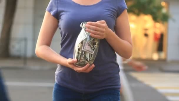 Vrouw met een glazen pot met dollars op een stad straat achtergrond — Stockvideo