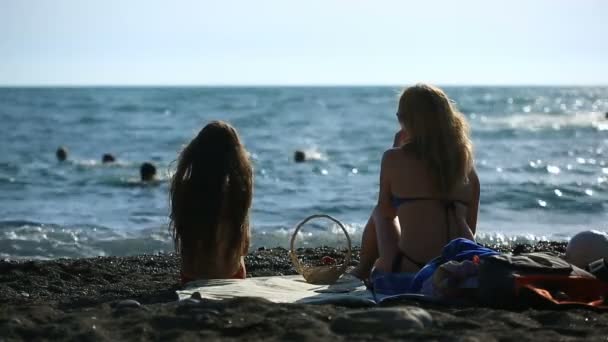 Mamá y su hija con el pelo largo en trajes de baño, comer frutas y bayas en una playa de mar sobre un fondo de olas — Vídeos de Stock