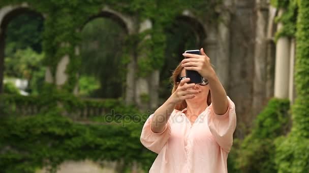 Une fille de touristes prend des photos de la belle collonade d'un vieux château tordu avec du lierre . — Video