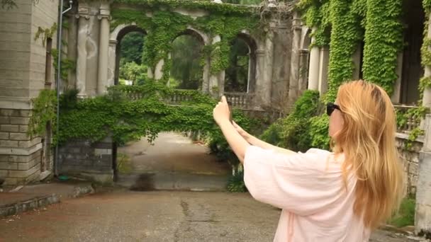 Une fille de touristes prend des photos de la belle collonade d'un vieux château tordu avec du lierre . — Video