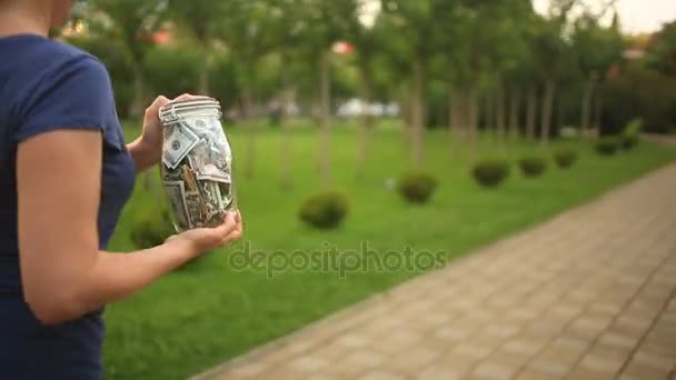 Γυναίκα κρατώντας ένα γυάλινο βάζο με δολάρια που τρέχει κάτω από ένα δρόμο της πόλης. Έννοια χρηματοδότηση, εκπτώσεις, πώληση. — Αρχείο Βίντεο
