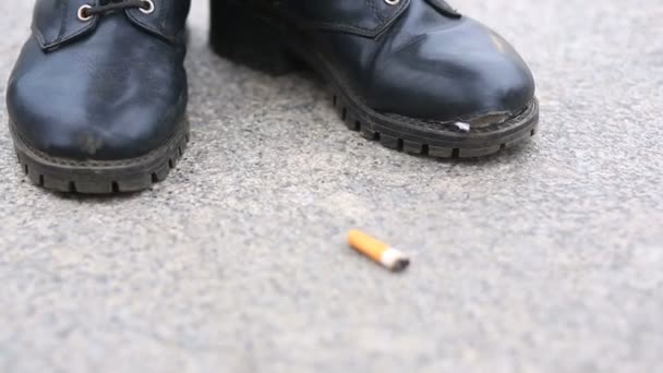 En man i slitna, trasiga stövlar på snörning står mitt på gatan bredvid en cigarettfimp — Stockvideo