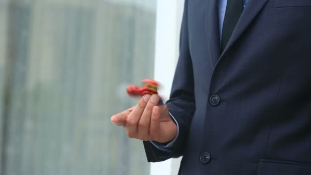 Veelkleurige, rood-geel-blauw hand spinner of fidgeting spinner, roterende op mans hand. Man in een pak spinnen een fidget spinner op straat — Stockvideo