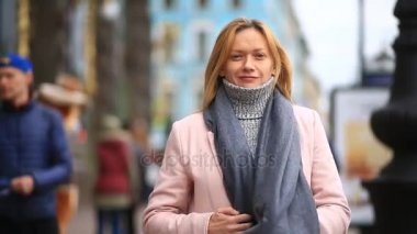 Bir pembe ceket ve kazak yorgun bir kadın kalabalık bir sokak ortasında duruyor ve soğuktan küçülür