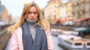 Bir pembe ceket ve kazak yorgun bir kadın kalabalık bir sokak ortasında duruyor ve soğuktan küçülür