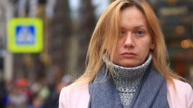 Bir pembe ceket ve kazak yorgun bir kadın kalabalık bir sokak ortasında duruyor ve soğuktan küçülür