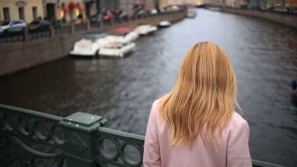 Una mujer con un abrigo se para en un puente y mira hacia el agua negra. Quiere suicidarse. — Vídeo de stock