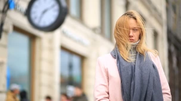 Una mujer con un abrigo rosa y suéter está de pie en medio de una calle llena de gente cerca del reloj y esperando la reunión — Vídeos de Stock