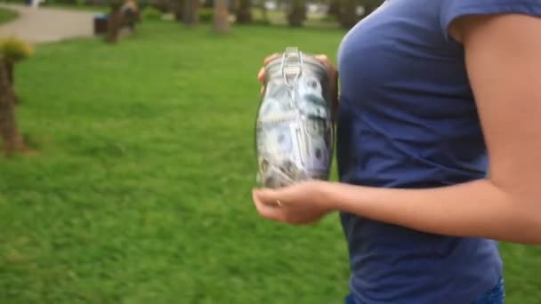 Bir cam kavanoz dolar şehir sokak arka plan üzerinde tutan kadın — Stok video