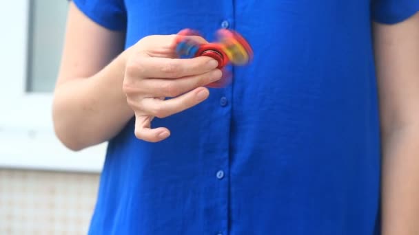 Multicolored, red-yellow-blue hand spinner, or fidgeting spinner, rotating on mans hand. Woman spinning a Fidget Spinner on the street — Stock Video