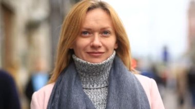 Bir pembe ceket ve kazak yorgun bir kadın kalabalık bir sokak ortasında duruyor ve soğuktan küçülür