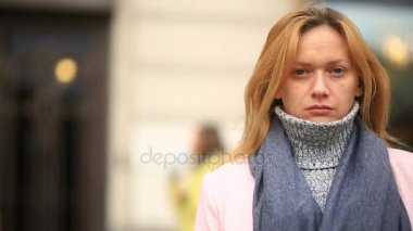 Bir pembe ceket ve kazak yorgun bir kadın kalabalık bir sokak ortasında duruyor ve soğuktan küçülür