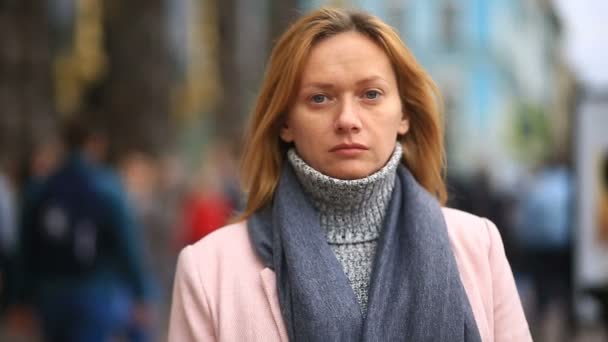 En trött kvinna i en rosa kappa och tröja står mitt i en trång gata och krymper från kylan — Stockvideo