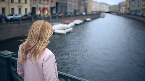 Μια γυναίκα σε ένα παλτό στέκεται σε μια γέφυρα και κοιτάζει κάτω στο μαύρο νερό. Θέλει να αυτοκτονήσει — Αρχείο Βίντεο
