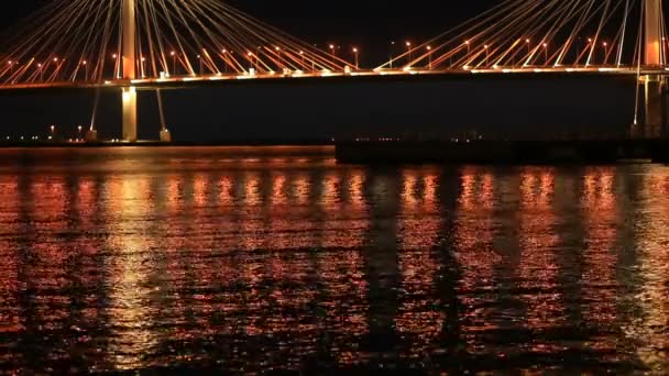 Ночью на воде мерцают огни города. Кабельный мост через реку — стоковое видео