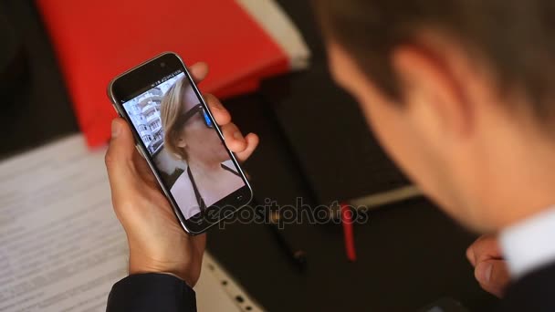 Ein Geschäftsmann im Anzug sitzt im Büro an seinem Schreibtisch und führt einen Videochat mit einem Mädchen am Strand. sie trägt einen Badeanzug und lädt ihn ein, sich ihr anzuschließen — Stockvideo