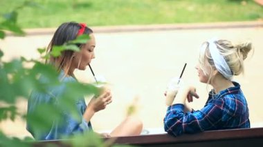 İki arkadaş şehir parkta bir bankta oturmak ve bir milkshake tek kullanımlık bir bardak içki