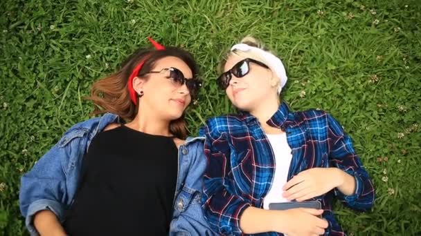 Due ragazze carine allegre fanno selfie al telefono, sdraiate sulla radura verde del parco cittadino. vista dall'alto — Video Stock