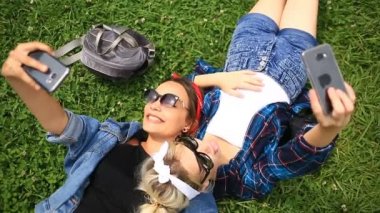Selfie telefonda Şehir Parkı yeşil glade üzerinde oturan iki neşeli şirin kız arkadaşım var