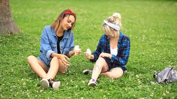 Dos novias alegres sentadas en el césped en el parque de la ciudad y comiendo helado — Vídeos de Stock