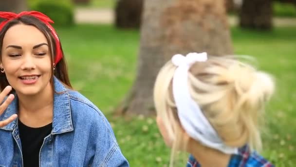 Dos novias alegres sentadas en el césped en el parque de la ciudad y comiendo helado — Vídeos de Stock