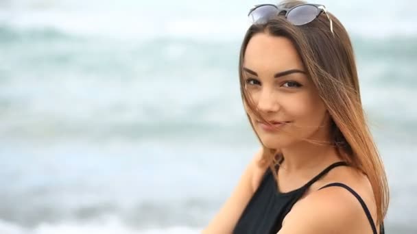 Mooie jonge brunette meisje met bruine ogen, schattige glimlachen en kijken naar de camera op een achtergrond van zee golven — Stockvideo