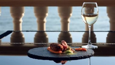 Gurme restoranda yemekler. Yakın çekim. Tavşan eti yeşil buğday bir garnitür ile gelen pirzola. Bir bardak beyaz şarap. Sahil Restoran Deniz Manzaralı