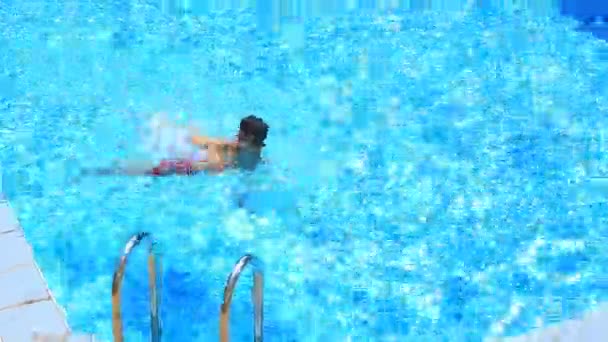 Das Kind schwimmt im blauen Wasser des Pools. Blick von oben. — Stockvideo