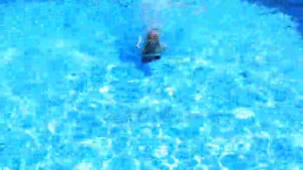 El niño está nadando en el agua azul de la piscina. vista desde arriba. La chica se sumerge en el agua — Vídeos de Stock