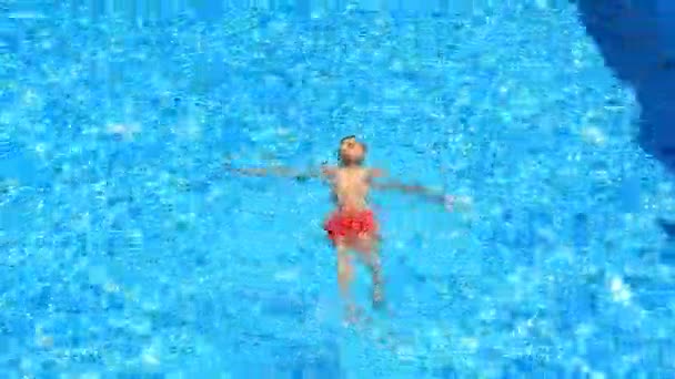 Das Kind schwimmt im blauen Wasser des Pools. Blick von oben. — Stockvideo