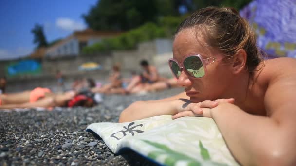 Frau sonnt sich am Strand auf Steinen liegend — Stockvideo