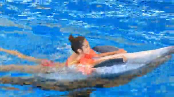 Дитя и дельфины. Девочка-подросток плавает с дельфином, держащимся за его плавники — стоковое видео