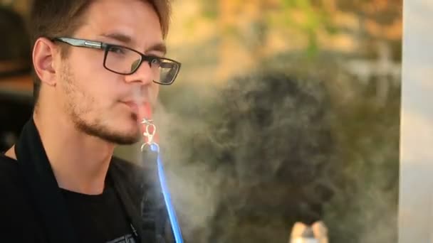 Junger intelligenter Mann, der Wasserpfeife raucht. in einem Open-Air-Restaurant — Stockvideo