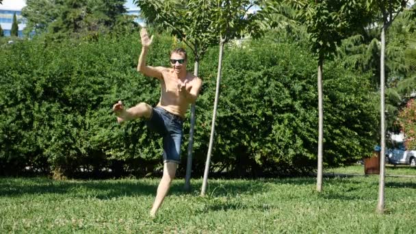 Молодий щасливий хлопець з голим торсом танцює сучасний балет і качається в літньому парку. повільний час — стокове відео
