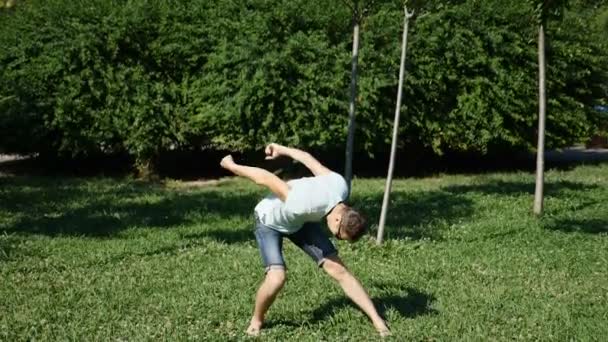 Een jonge gelukkige kerel moderne ballet en wacking dansen in een zomer-park. slow-mo — Stockvideo