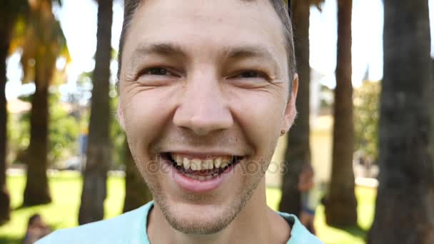 여름 공원에서 젊은 잘생긴 남자가 카메라를 보고 웃는 다. 슬로우 모션 — 비디오