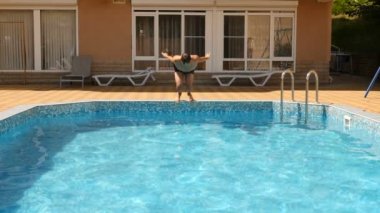 Bir adam mavi su ile havuz içine dalış. Su sıçramalarına farklı yönlere sinek. Ağır çekim