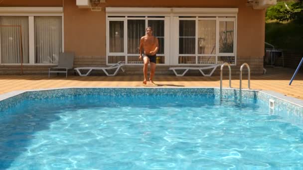 Ein Mann taucht in den Pool mit blauem Wasser. Spritzer fliegen in verschiedene Richtungen. Zeitlupe — Stockvideo