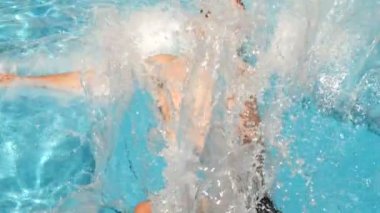 Bir adam mavi su ile havuz içine dalış. Su sıçramalarına farklı yönlere sinek. Ağır çekim