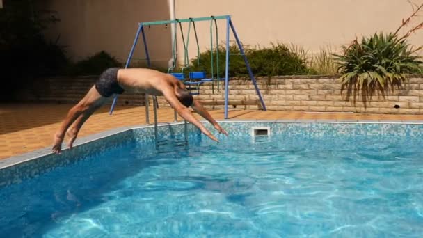 Człowiek nurkuje się w basenie z błękitną wodą. Odpryskami latają w różnych kierunkach. Zwolnionym tempie — Wideo stockowe