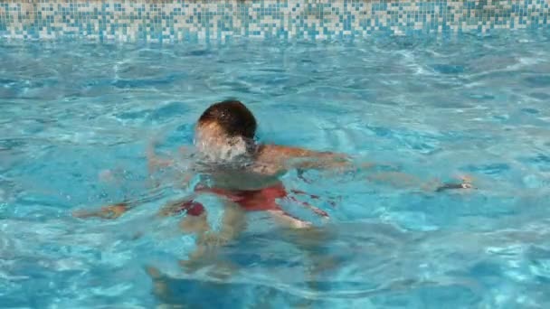 Мужчина ныряет в бассейн с голубой водой. Всплески разлетаются в разные стороны. Медленное движение — стоковое видео