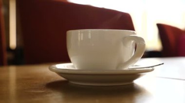 Arka planda hareketli bulanık insanlarla kahve dumanı tüten sıcak bir fincan.